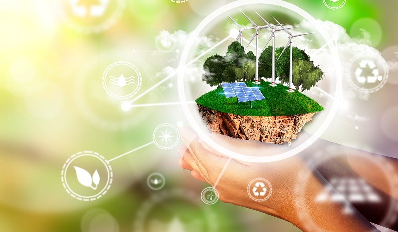 Women´s hand with island with solar panels, wind fans, trees and clouds. Energy efficiency concept.